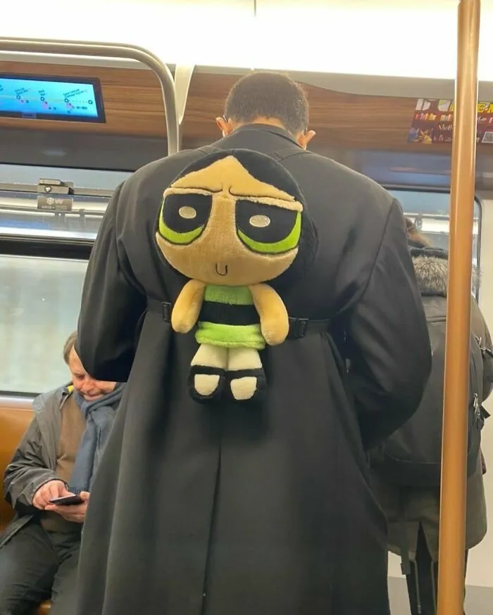 Man wearing black coat with a plush toy backpack in a subway, one of the weirdest things seen on the streets of Brussels.
