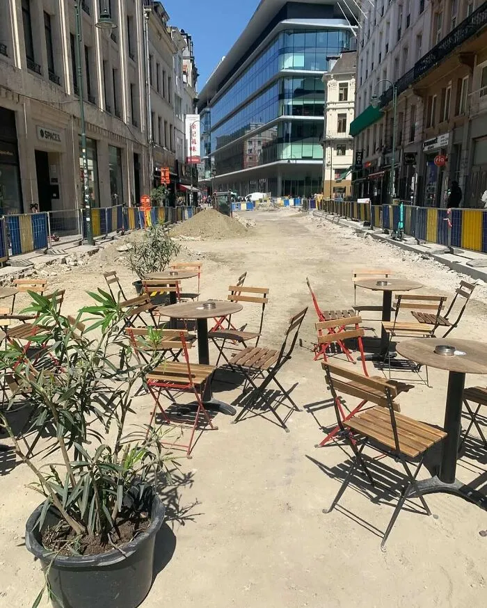 Outdoor café tables and chairs arranged on a dusty street under construction in Brussels, showcasing weird street scenes.