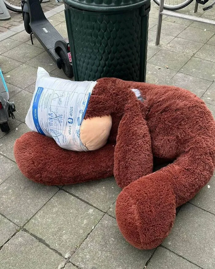 Giant plush monkey with head inside a plastic bag lying on the sidewalk in Brussels, showing weird street scene.