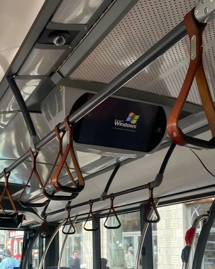 Bus interior in Brussels showing leather hand straps and a Windows boot screen on a ceiling-mounted monitor.