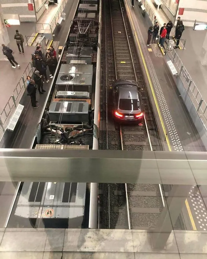 Black car stuck on train tracks next to a tram at a busy Brussels station, showcasing weirdest street scenes.