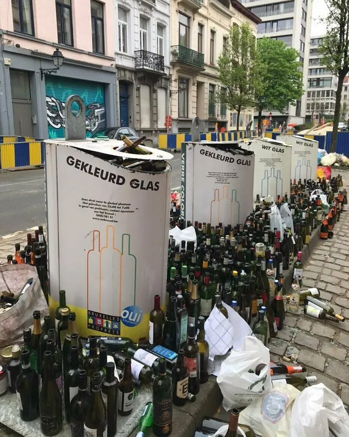 Street scene in Brussels showing a large collection of glass bottles scattered around recycling bins, capturing weird street clutter.