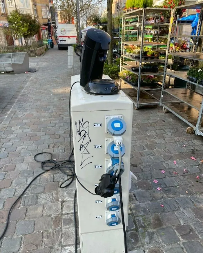 Coffee maker plugged into an outdoor power strip on a cobblestone street, one of the weirdest things seen on Brussels streets.