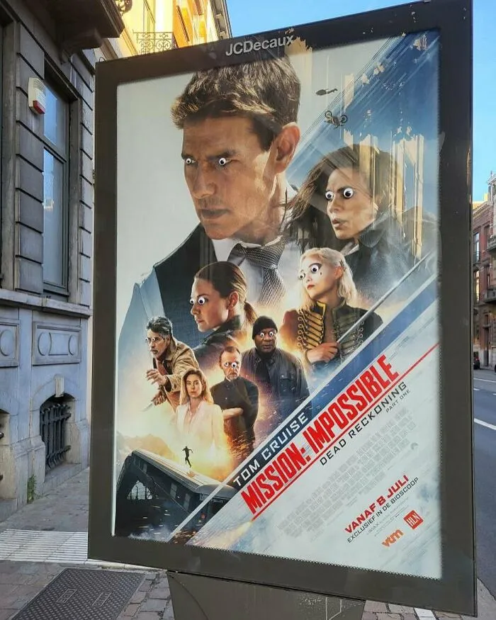 Mission Impossible movie poster on Brussels street with added googly eyes, showcasing weird and unhinged street art.