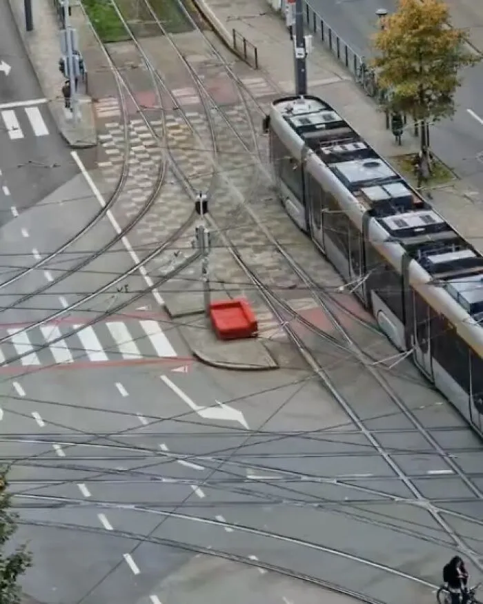 Complex tram tracks and wires intersecting on the streets of Brussels with a modern tram and a cyclist nearby.