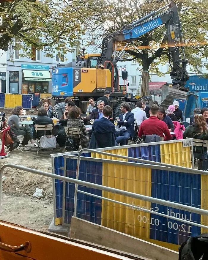 People dining outdoors next to a construction site with heavy machinery in the streets of Brussels.