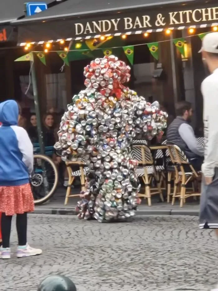 Person in a costume made entirely of crushed cans on the streets of Brussels, showcasing one of the weirdest street sights.
