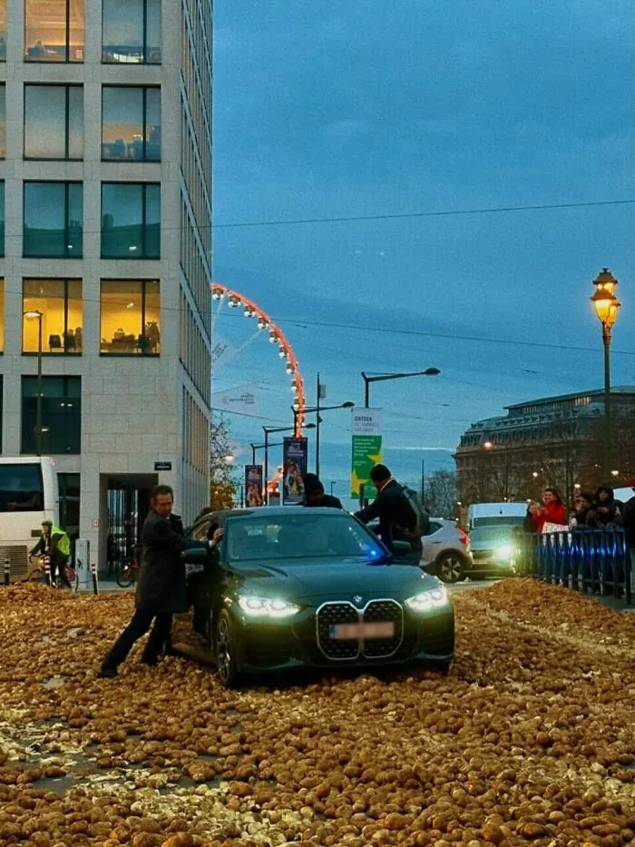 Car stuck in a sea of potatoes on the streets of Brussels with people helping around the unusual scene.