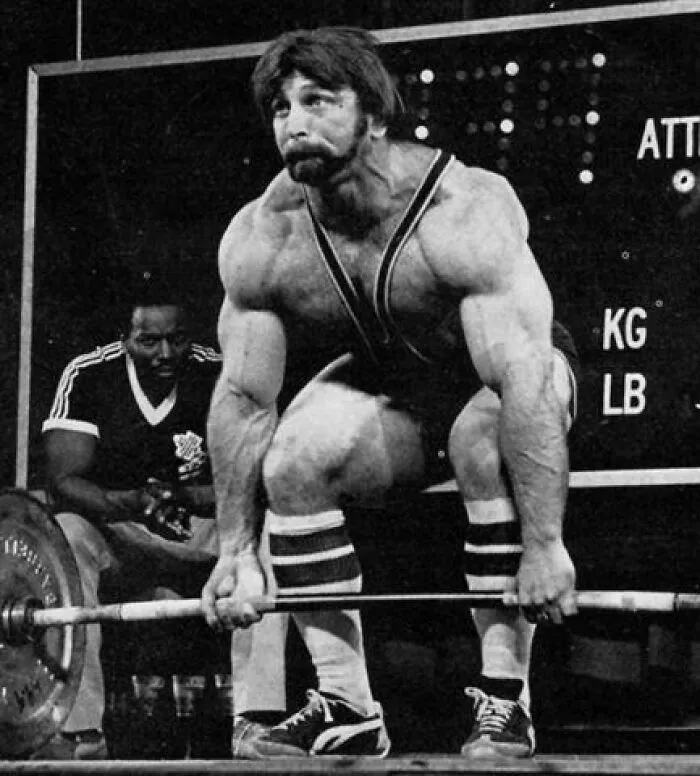 Muscular man lifting heavy barbell during weightlifting event, illustrating a photo that wasn’t what it seemed.