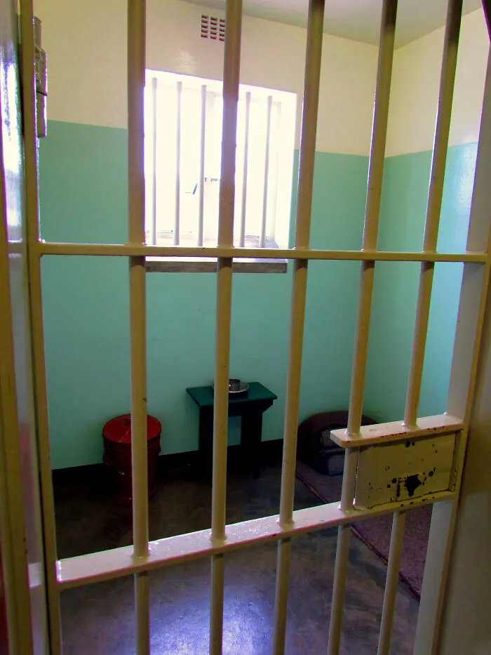 View of a small jail cell with bars, simple furniture, and a window, representing disappointing tourist attractions.