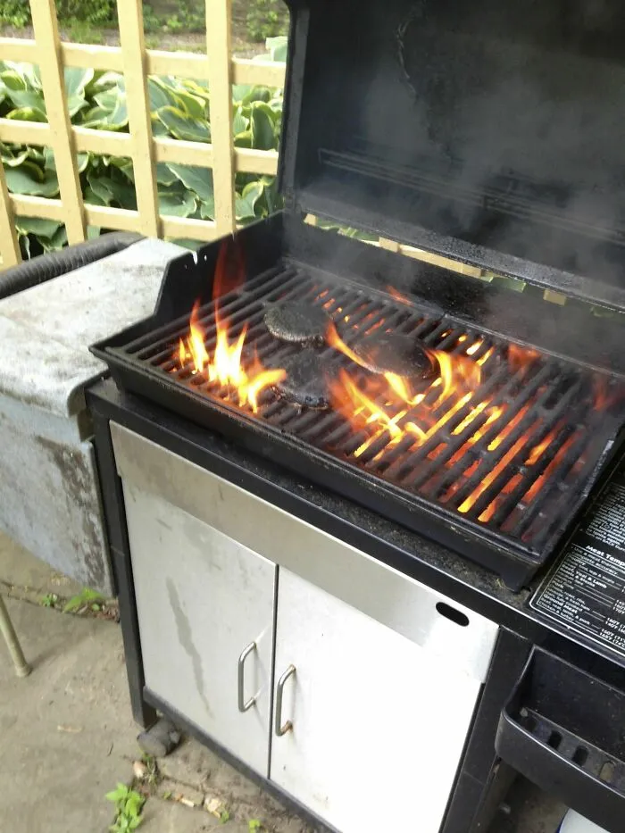 Parrilla con hamburguesas quemadas y llamas, uno de los errores divertidos de esposas y novias en días ordinarios.