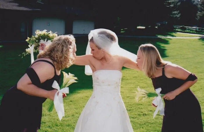 Bride in wedding dress striking a funny pose while bridesmaids lean in, creating an awkward wedding photo moment outdoors.