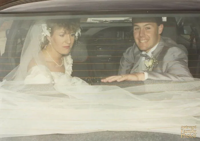 Bride and groom sitting awkwardly in the backseat of a car, captured in an awkward wedding photo moment.