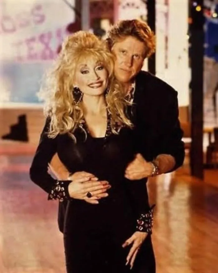 Couple hugging on a dance floor, woman with big blonde hair in a black dress and man behind her, It Rained Frogs