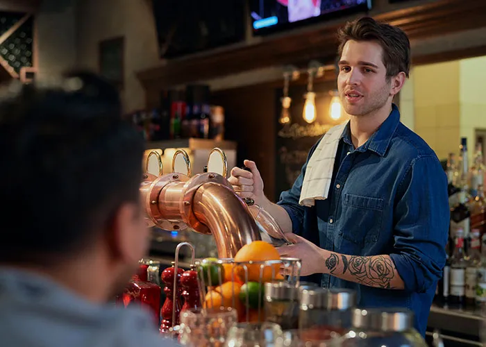 Man with a tattoo serving drinks behind the bar, a sad farewell atmosphere reflecting heartbreaking airport goodbyes.