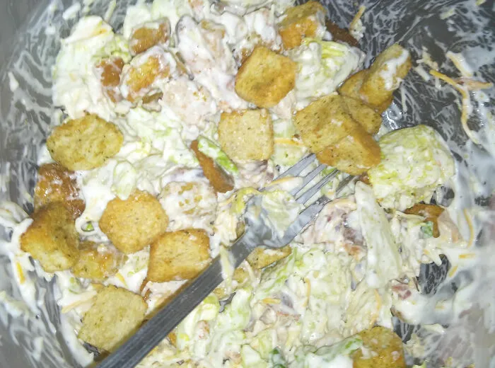 Close-up of a messy salad bowl with creamy dressing and croutons, illustrating buffet employees’ disgusting display of gluttony.