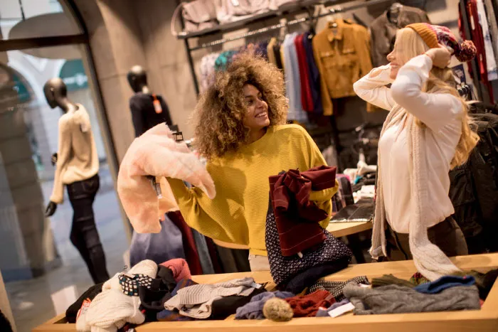 Two women shopping for clothes, sharing opinions and enjoying a lively conversation in a boutique setting.