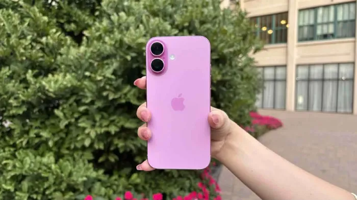 Hand holding a pink iPhone outdoors with green bushes and building windows in the background, illustrating boomer opinions.