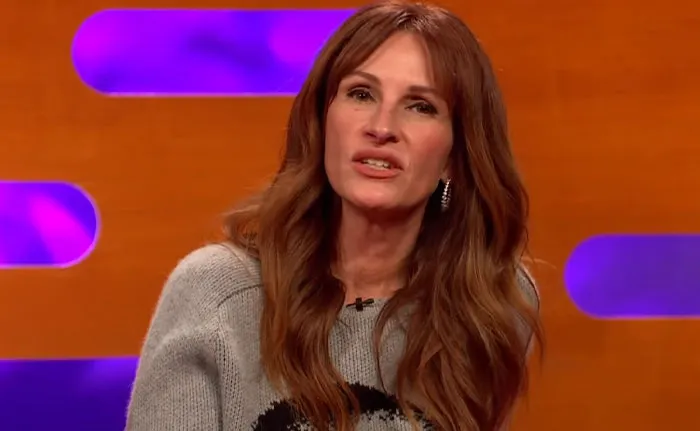 Female celebrity with long hair speaking on a television talk show about celebrity infidelity scandals.