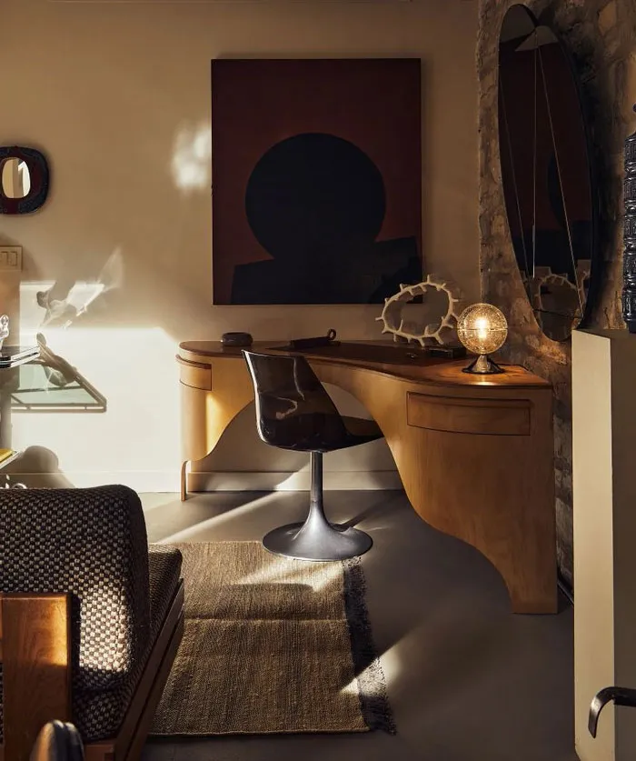 Cozy interior design idea featuring a wooden desk, modern chair, abstract art, and warm ambient lighting in a stylish room.