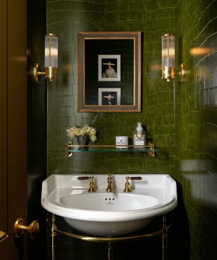 Small bathroom with cool interior design ideas featuring a white sink, green textured walls, brass fixtures, and elegant lighting.