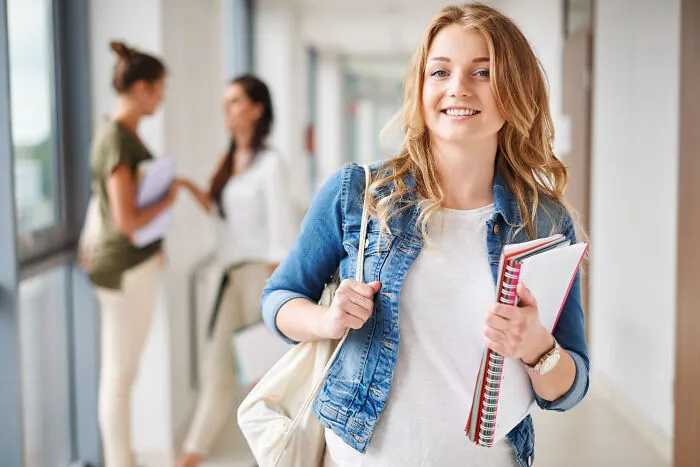 Smiling female student in school hallway holding notebooks, symbolizing high school secrets and late discoveries