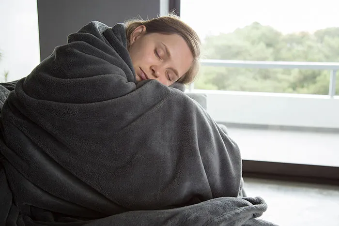 A woman wrapped in a grey blanket with eyes closed, symbolizing a feeling her intelligence was sharp and overwhelming.