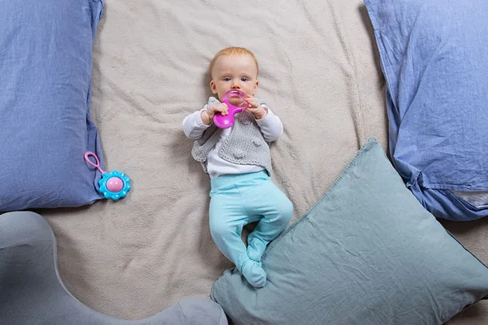 Baby lying on bed surrounded by pillows and toys, capturing a moment of sharp intelligence and curiosity.