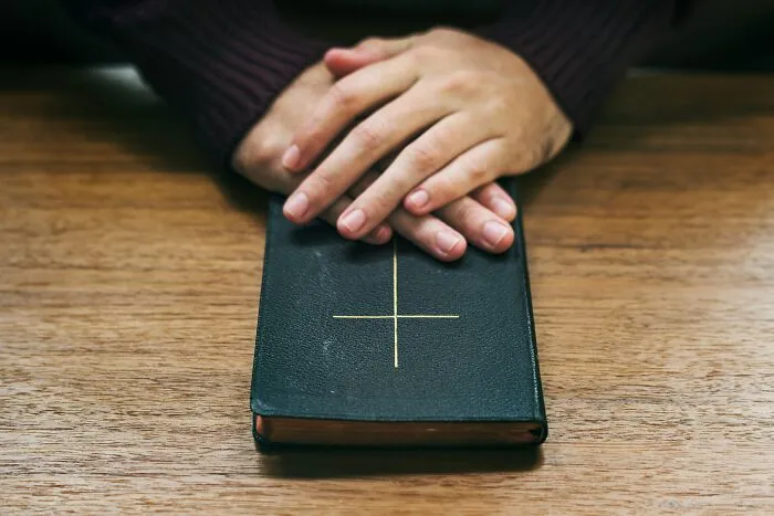 Hands resting on a closed book with a cross, symbolizing reflection on worst coworkers making work feel like a nightmare.