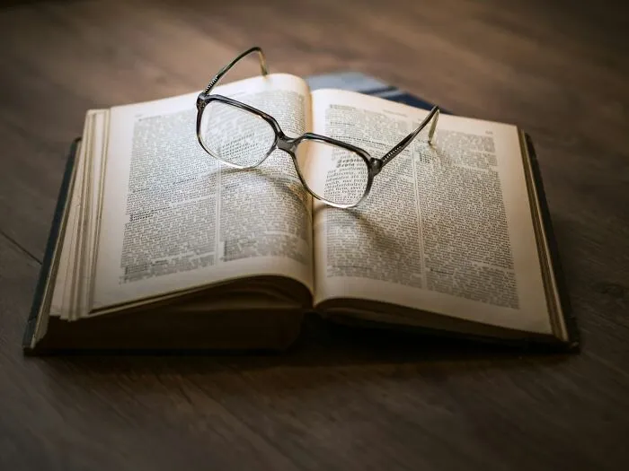 Open book with reading glasses resting on top, representing cultural insights from people sharing things normal in their country but offensive elsewhere.