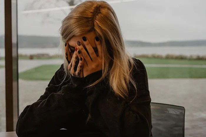 Woman with blonde hair covering her face indoors, reflecting on women’s bodies and experiences they wish were studied properly.