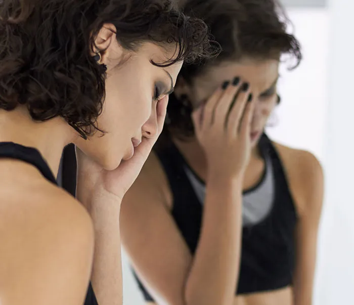 Woman in black top looking distressed and holding her head, reflecting struggles with understanding women's bodies and health.