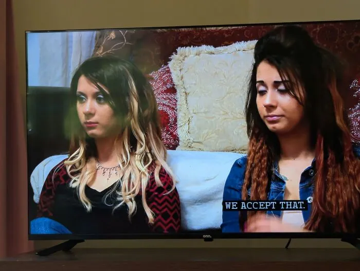 Two women with disastrous hairstyles sitting on a couch, highlighting questionable hair choices in casual setting.