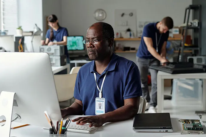 Middle-aged man focused on computer work in a modern office with colleagues, showcasing gifted kids potential theme.