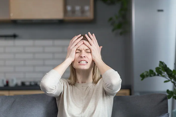 Woman sitting on couch in kitchen, holding head with hands, expressing frustration or stress about gifted kids potential.