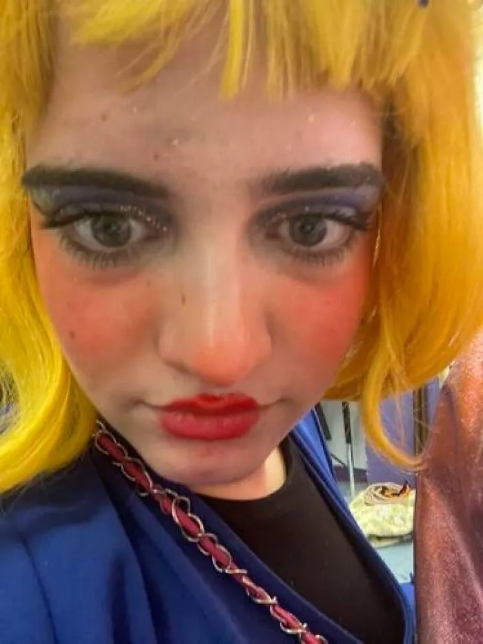 Close-up of a person with theatrical stage makeup featuring bold colors and a bright yellow wig.