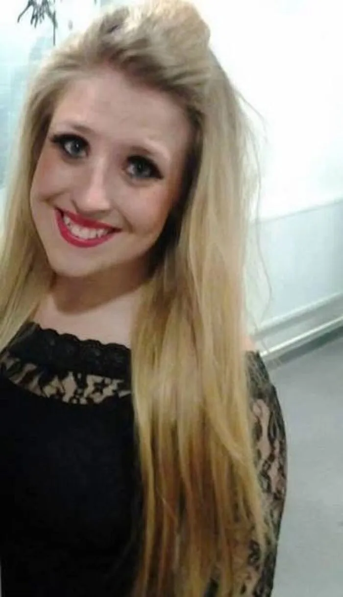 Young woman with dramatic stage makeup wearing a black lace dress smiling indoors, showcasing stage makeup look.