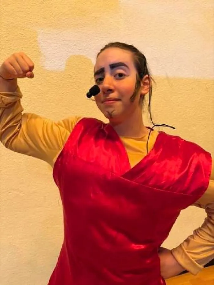 Person in red stage costume with exaggerated makeup flexing arm, illustrating stage makeup magical and mildly cursed looks.