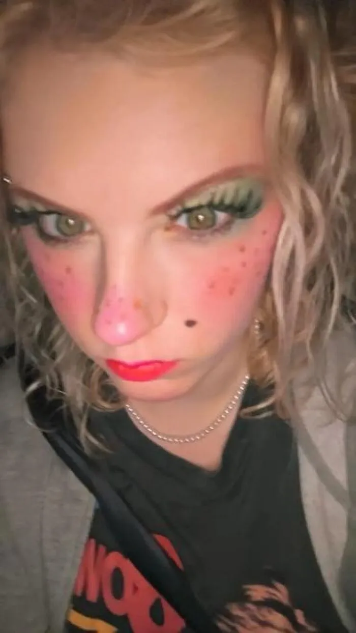 Close-up of a person with exaggerated stage makeup featuring bright eyeshadow, red lips, and pink freckles for a magical look.