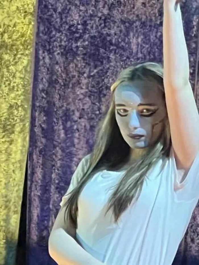 Young woman with stage makeup looking magical on stage with dramatic lighting and dark background curtain.
