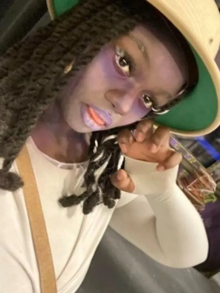 Person with dramatic stage makeup and hat striking a pose, showcasing magical stage makeup look with a mildly cursed vibe.
