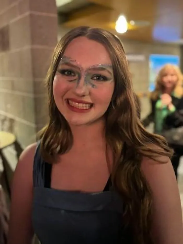 Young woman smiling with magical stage makeup featuring glitter and bold eyebrows, showcasing artistic stage makeup effects.