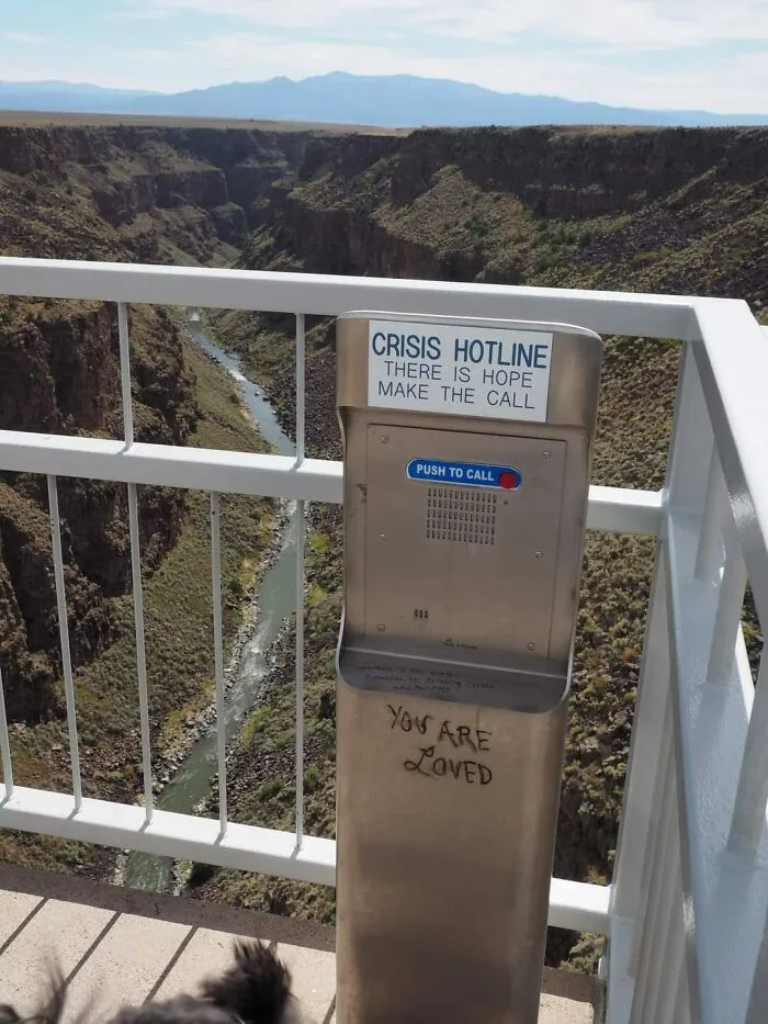 Crisis hotline call box on bridge over canyon with river, featuring message of hope in a dystopia setting.