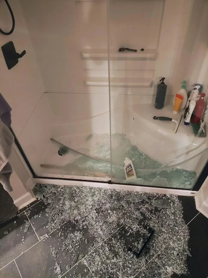 Broken glass shower door shattered on bathroom floor with shampoo bottles inside, showing unfortunate events that make you feel better.