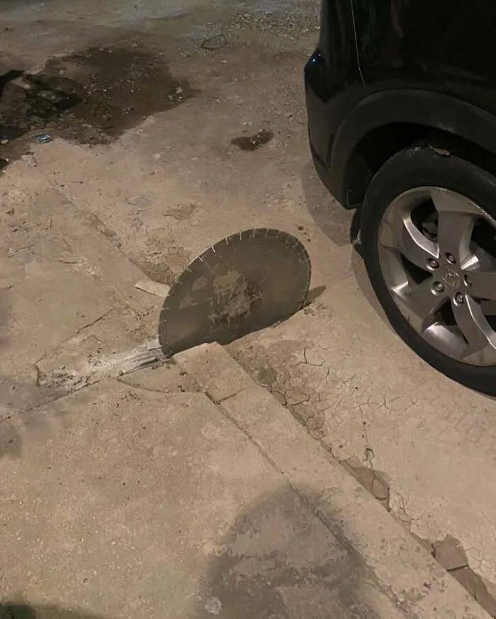 Circular saw blade embedded in the cracked street pavement near a parked car, one of the weirdest things found in the streets.