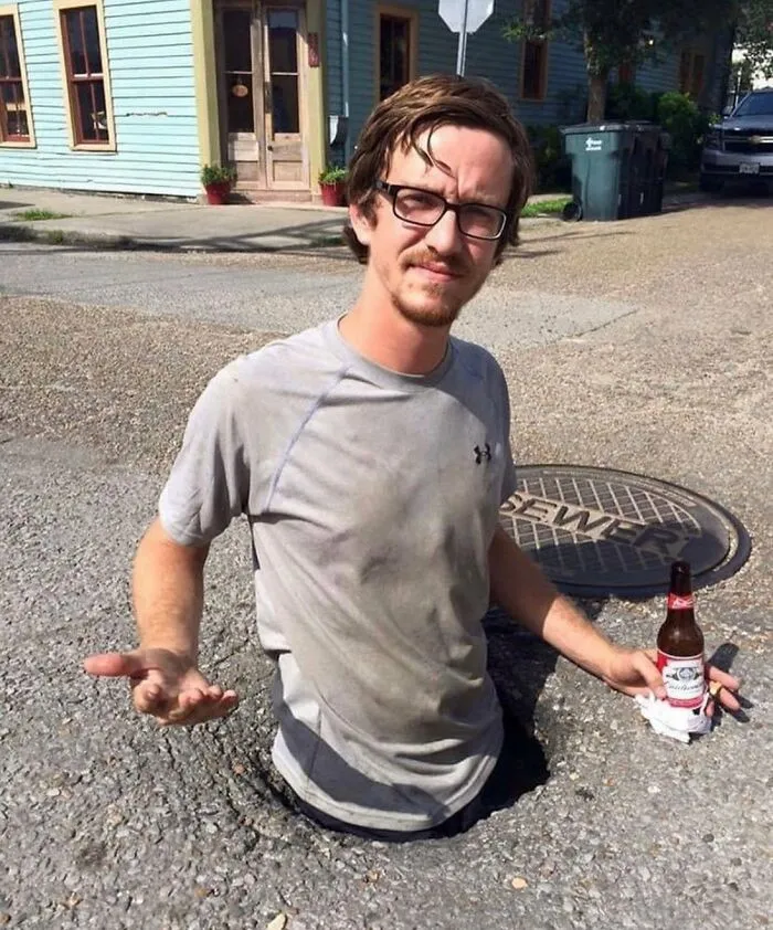 Man partially stuck in street hole holding a beer bottle, an example of weird things found in the streets.