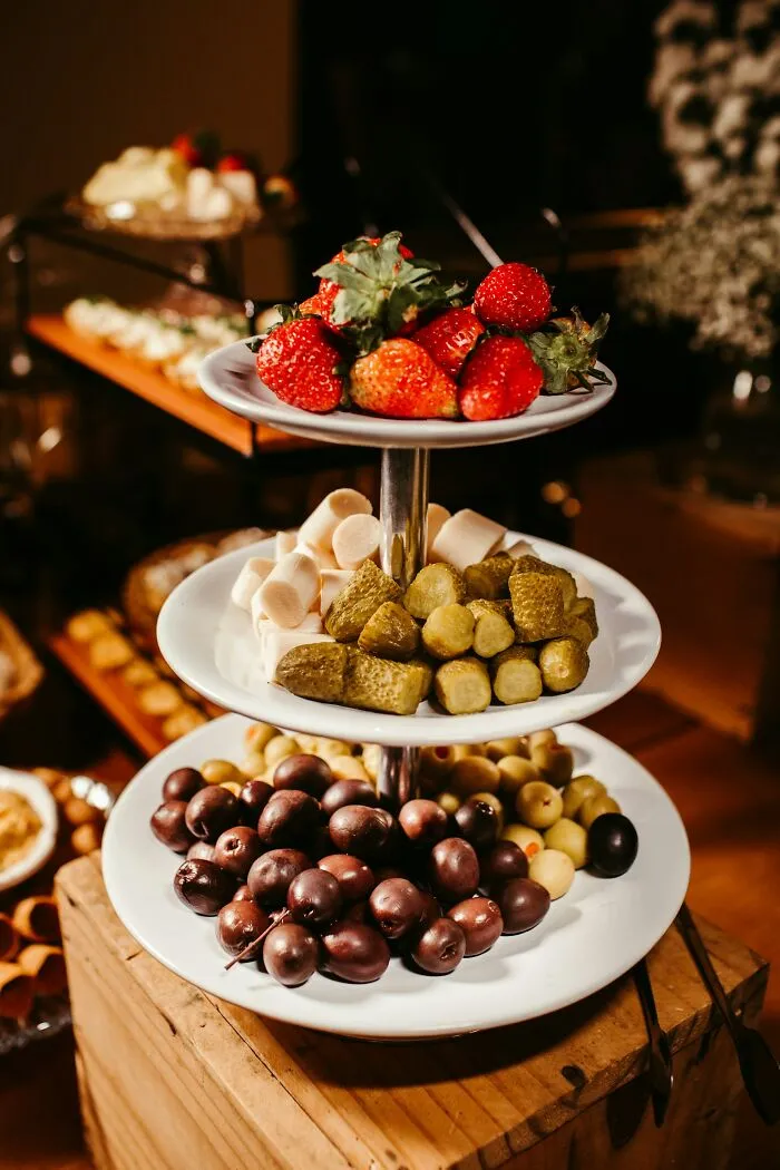 Three-tiered serving tray with strawberries, pickles, marshmallows, and olives, illustrating rich people far from reality.