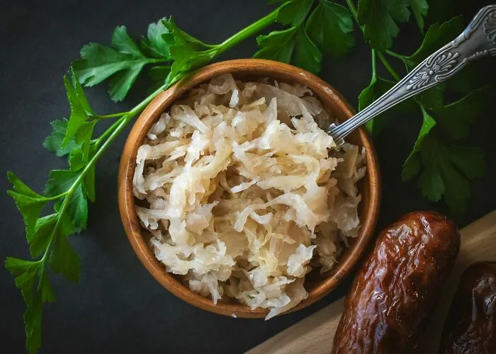 Bowl of sauerkraut with fresh parsley and sausages on a dark surface illustrating shipping containers concepts.