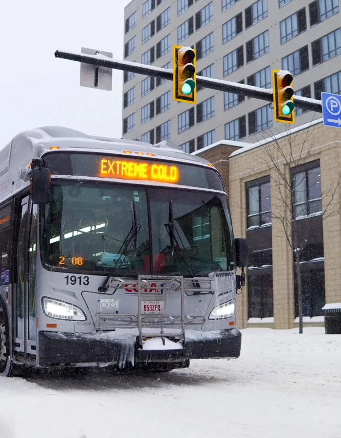Bus covered in snow and icicles during a snowstorm with extreme cold warning in an urban U.S. setting.