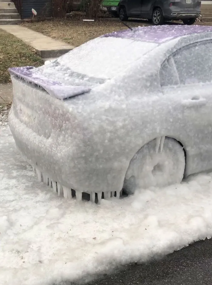 Car covered in thick ice and snow during a snowstorm hitting the U.S., creating icy icicles around the wheels and body.